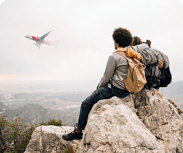 Two hikers on a clifftop rock watching a plane fly over the valley